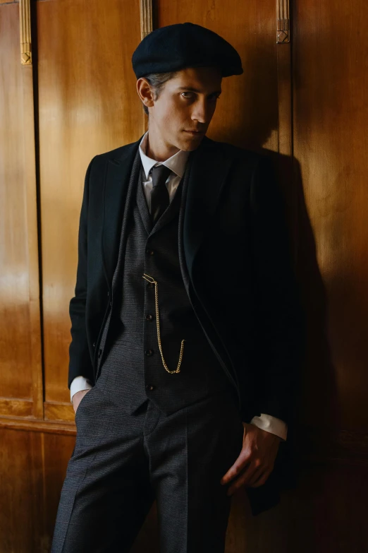 a man in a suit and hat leaning against a wall, an album cover, inspired by August Sander, unsplash, renaissance, neck chains, robert sheehan, 3-piece-suit, smooth panelling