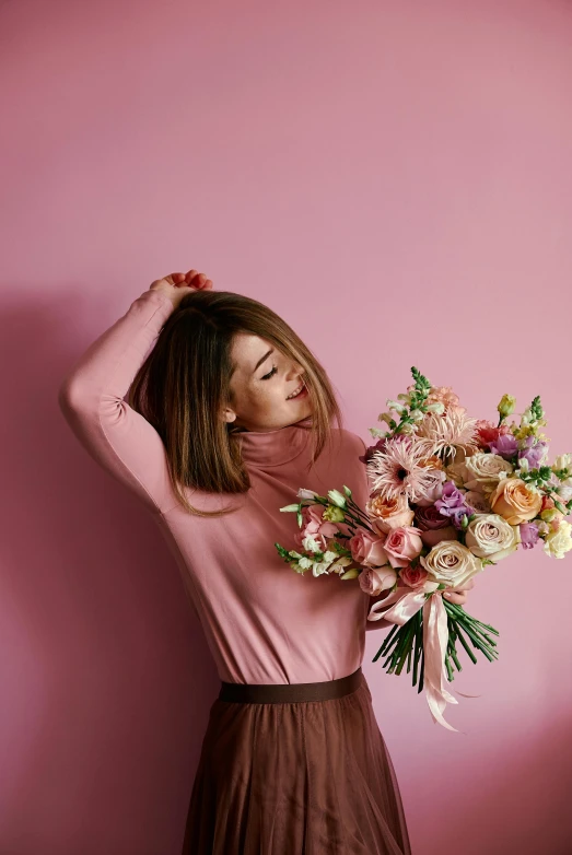 a woman holding a bouquet of flowers against a pink wall, by Julia Pishtar, trending on pexels, made of flowers, pink shirt, brown and pink color scheme, embracing