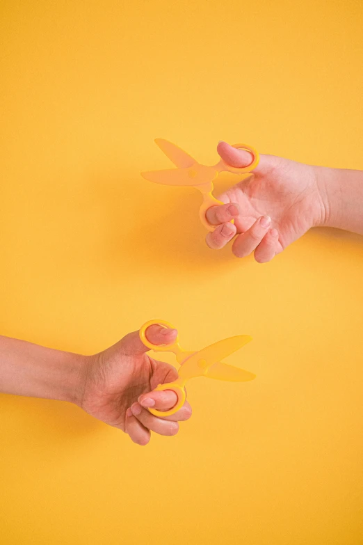 a pair of hands holding a pair of scissors, by Adam Marczyński, new objectivity, yellow-orange, toys, dueling, minimalist photorealist