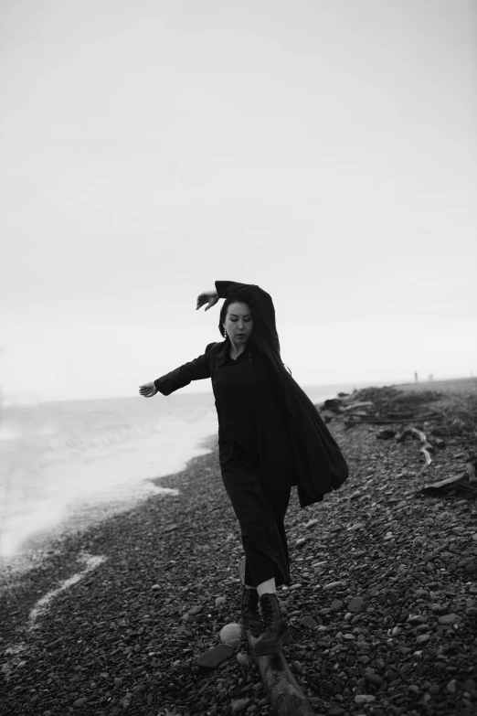 a woman standing on top of a beach next to the ocean, a black and white photo, by Clifford Ross, wearing black wizard robes, running freely, wu liu, rainy