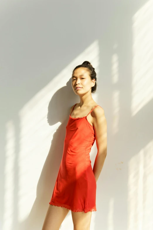 a woman in a red dress leaning against a wall, by Lucette Barker, pexels contest winner, gutai group, soft grey and red natural light, wearing a camisole, asian sun, alexandria ocasio cortez