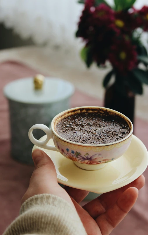 a person holding a cup of coffee on a saucer, by Lucia Peka, pexels contest winner, hurufiyya, mixture turkish and russian, fully chocolate, vintage soft grainy, round-cropped