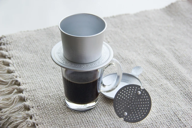 a cup of coffee sitting on top of a table, grey and silver, in style of lam manh, single, grey