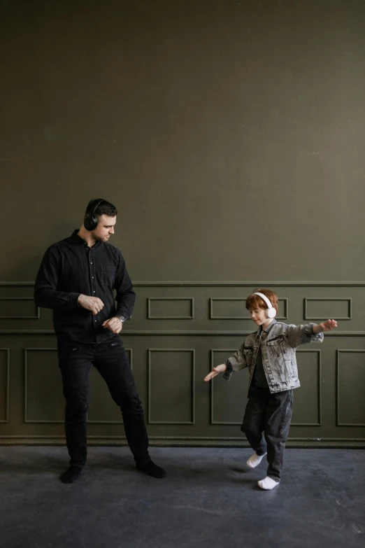 a man standing next to a little boy in a room, by Nina Hamnett, pexels contest winner, visual art, he is dancing, darkslategray wall, smooth panelling, olive