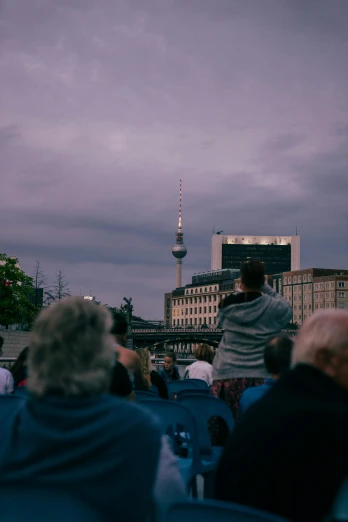 a crowd of people sitting next to each other, a photo, pexels contest winner, berlin secession, space ship in the distance, summer evening, the wise man is riding on top, audience