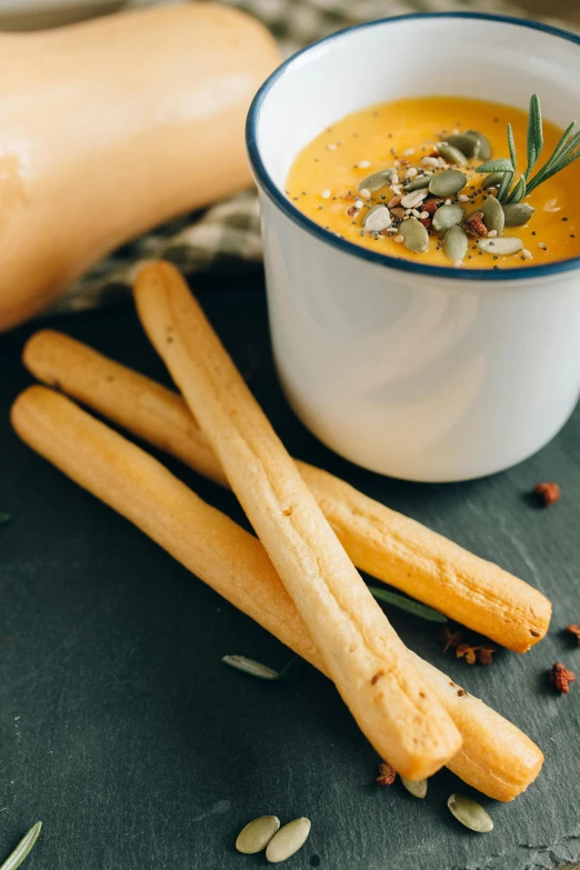 a bowl of soup and some breadsticks on a table, inspired by Géza Dósa, unsplash, square, mustard, dynamic closeup, halo