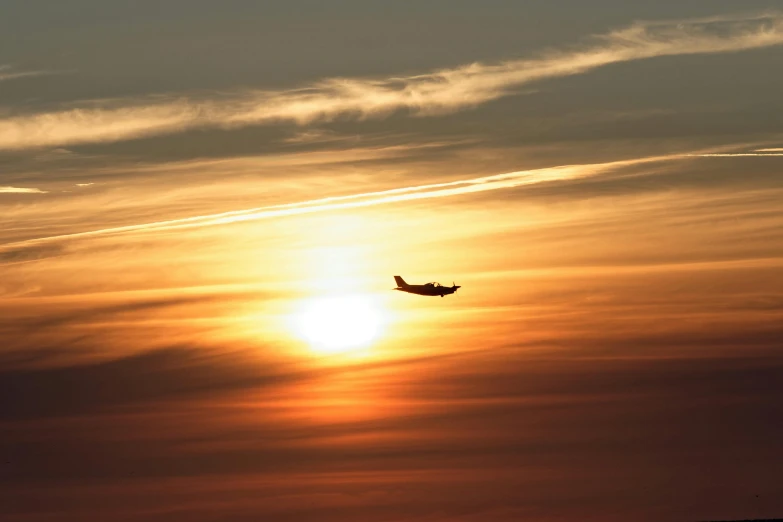 a large jetliner flying through a cloudy sky, by David Simpson, pexels contest winner, hurufiyya, nuclear sunset, winter sun, spitfire, in a sunset haze