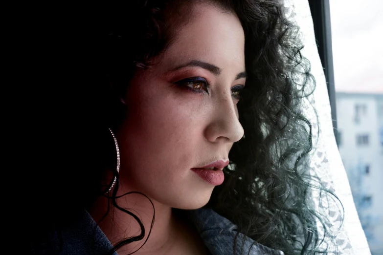 a close up of a woman looking out a window, an album cover, inspired by Amelia Peláez, cynthwave, with a black background, portrait mode photo, middle eastern skin