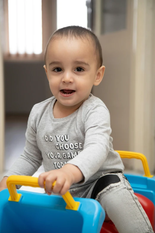 a little boy that is sitting on a toy car, walking towards the camera, activity play centre, grey, sam nassour