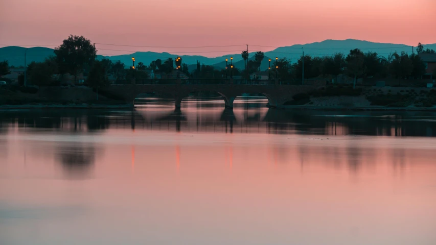 a body of water with a bridge and mountains in the background, pexels contest winner, romanticism, pink shadows, arizona, city twilight landscape, faded glow