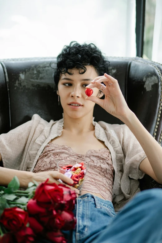 a woman sitting in a chair holding a bouquet of roses, inspired by Nan Goldin, pexels contest winner, romanticism, short black curly hair, attractive androgynous humanoid, snacks, heart shaped face