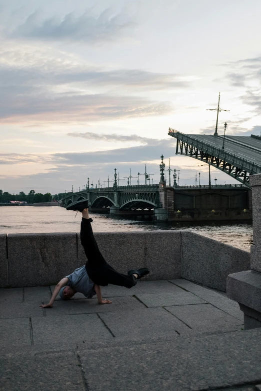 a person doing a handstand in front of a bridge, inspired by Illarion Pryanishnikov, kremlin, bent - over posture, julia hetta, in the evening