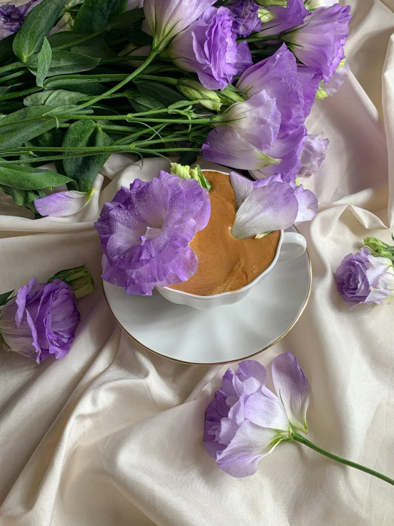 a white plate topped with purple flowers next to a cup of coffee, draped in purple and gold silk, dasha taran, datura, creamy skin