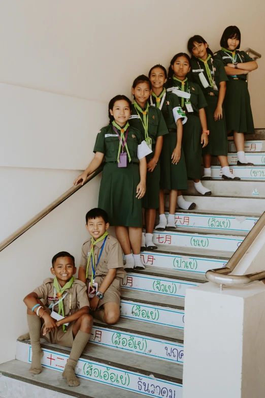 a group of children standing on a set of stairs, by Alison Geissler, danube school, thailand, scout boy, high school badge, green tonalities