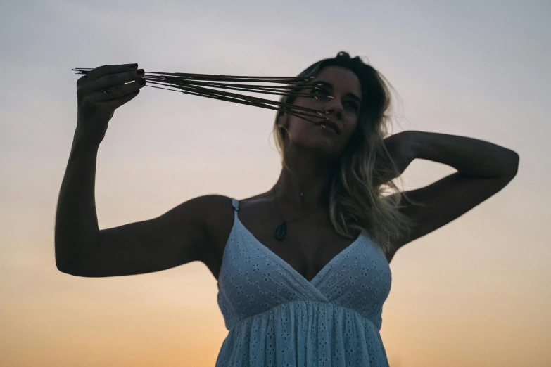 a woman holding a bunch of sticks in front of her face, pexels contest winner, happening, summer evening, her hair flowing down, profile image, slightly tanned