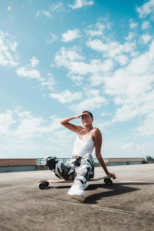 a woman sitting on a skateboard in a parking lot, in the sky, curated collections, camo, sunny sky