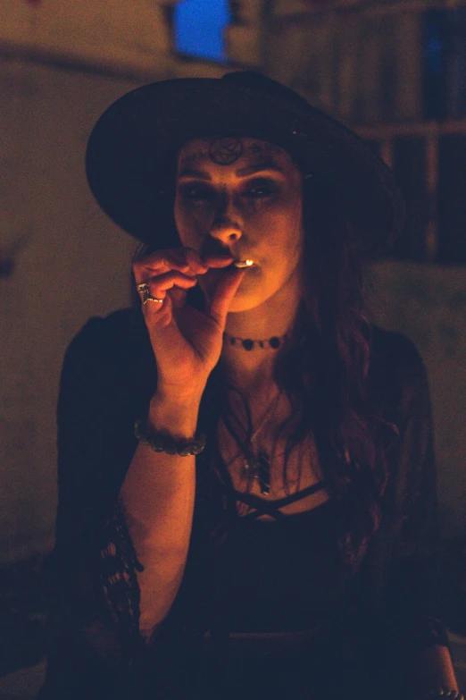 a woman in a hat smokes a cigarette, inspired by Elsa Bleda, pexels contest winner, renaissance, stoner rock concert, nighttime, oldwest, low quality photo