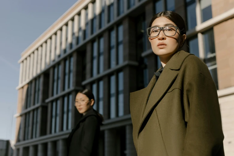 two women standing next to each other in front of a building, pexels contest winner, bauhaus, wearing a long coat, glasses |, chinese woman, worksafe. cinematic