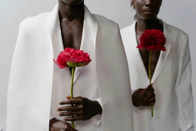 a couple of men standing next to each other holding flowers, inspired by Robert Mapplethorpe, trending on unsplash, romanticism, white robes, adut akech, crimson themed, ignant