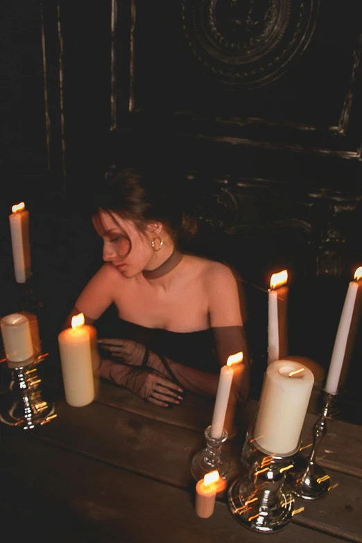 a woman sitting at a table with candles in front of her, inspired by Elsa Bleda, renaissance, vampire fashion, dark vhs gothic hearts, trending photo, corsets