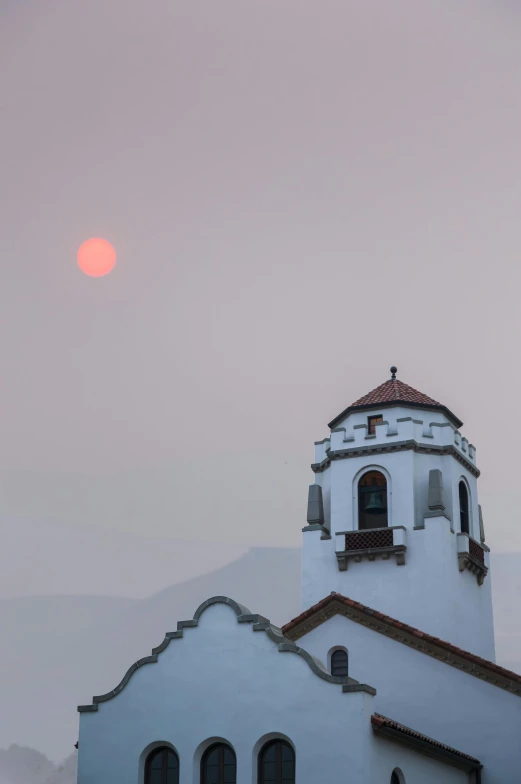 a large white building with a clock tower, a picture, by Neil Blevins, trending on unsplash, romanticism, red sun over paradise, smoky chimney, the city of santa barbara, shot with sony alpha