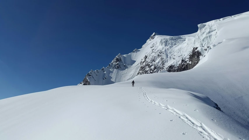 a person walking up the side of a snow covered mountain, clear blue skies, jordu schell, graeme base, profile image