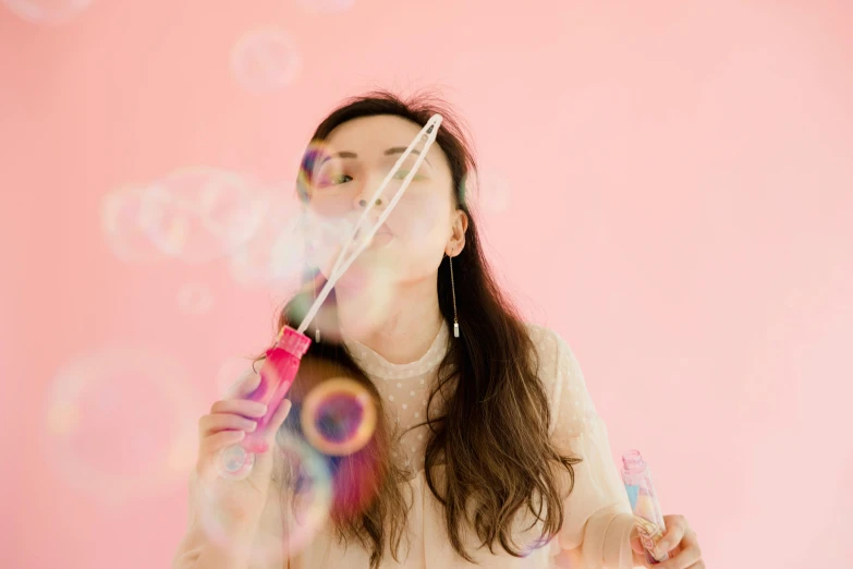 a woman blowing bubbles on a pink background, by Julia Pishtar, pexels contest winner, fan favorite, on white background, holding ego weapons, hey