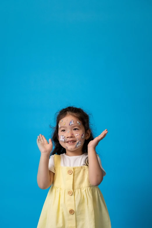 a little girl standing in front of a blue background, markings on her face, waving, gongbi, high quality photo