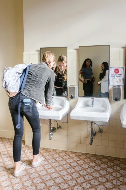 a woman standing in front of a row of sinks, happening, college girls, with a mirror, environmental shot, tyler