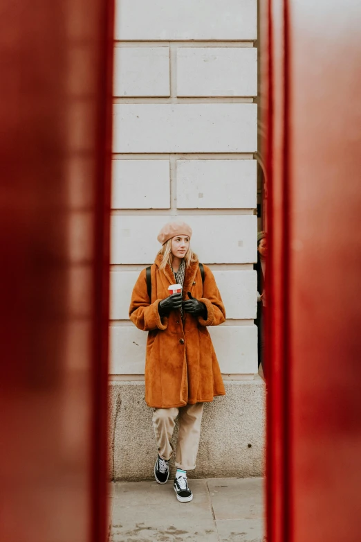 a woman standing in front of a red phone booth, by Tobias Stimmer, pexels contest winner, brown tuffle coat, teenager, caracter with brown hat, square