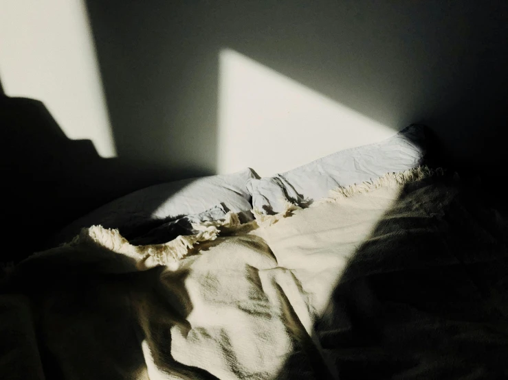 a bed sitting in a dark room next to a window, inspired by Elsa Bleda, unsplash, light and space, sun puddle, rinko kawauchi, ripped fabric, long cast shadows