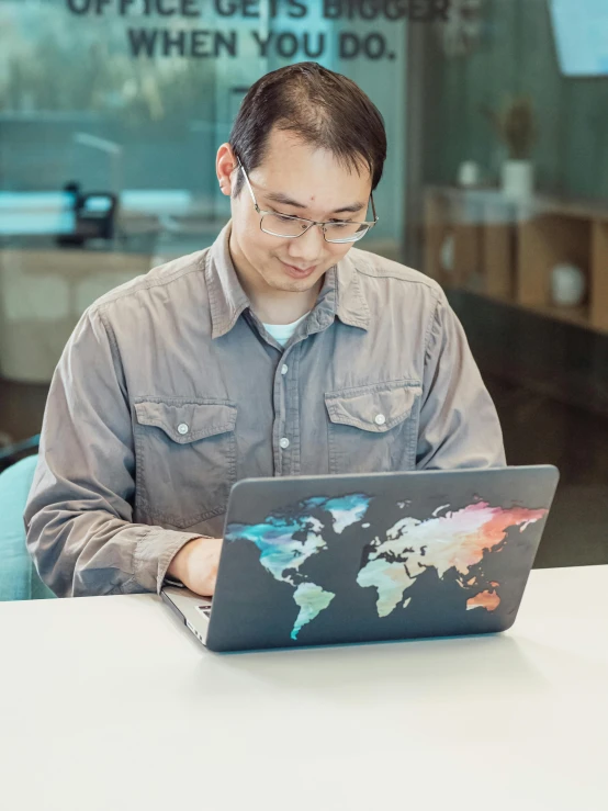 a man sitting at a table working on a laptop, a computer rendering, trending on unsplash, panfuturism, world map, ethnicity : japanese, 2 5 6 x 2 5 6 pixels, glowforge template