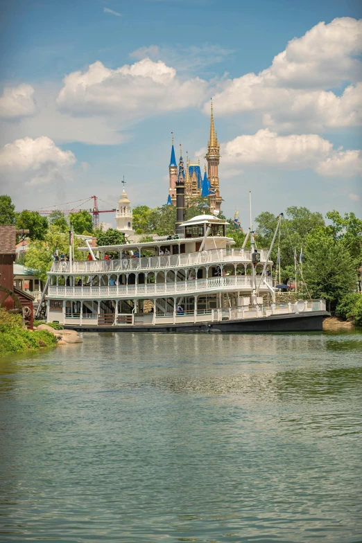 a large boat traveling down a river next to a castle, steamboat willy, victorian buildings, zoomed out view, square