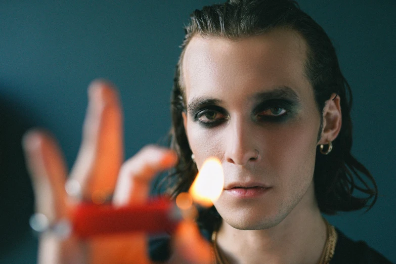 a close up of a person holding a lighter, an album cover, trending on pexels, bauhaus, handsome male vampire, casting a flame spell, with black sclera eyes, caleb from critical role