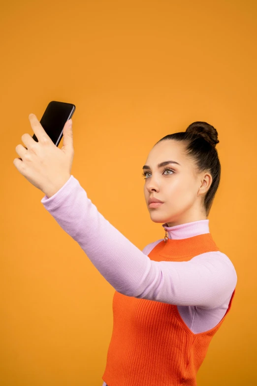 a woman taking a selfie with her cell phone, trending on pexels, orange gradient, wearing turtleneck, with a ponytail, solid background