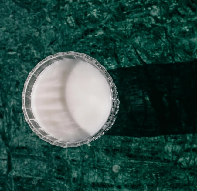 a glass of milk sitting on top of a table, unsplash, bauhaus, strong eggshell texture, dark green glass, shot on sony a 7, topdown