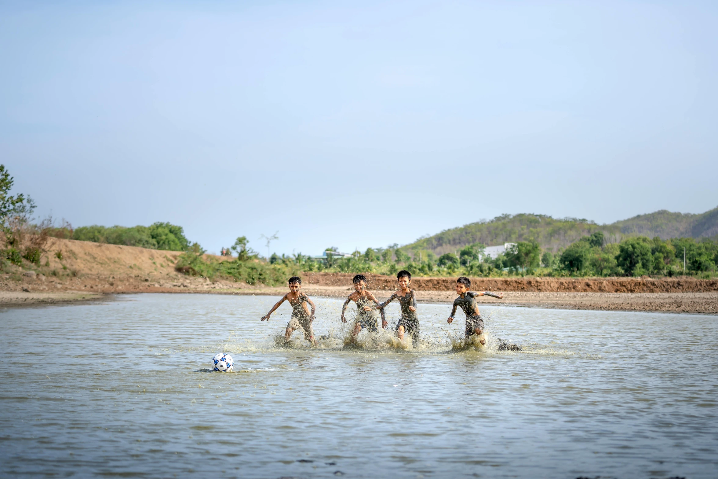 a group of boys playing soccer in the water, by Jesper Knudsen, unsplash contest winner, villagers busy farming, terracotta, nivanh chanthara, sunny day time