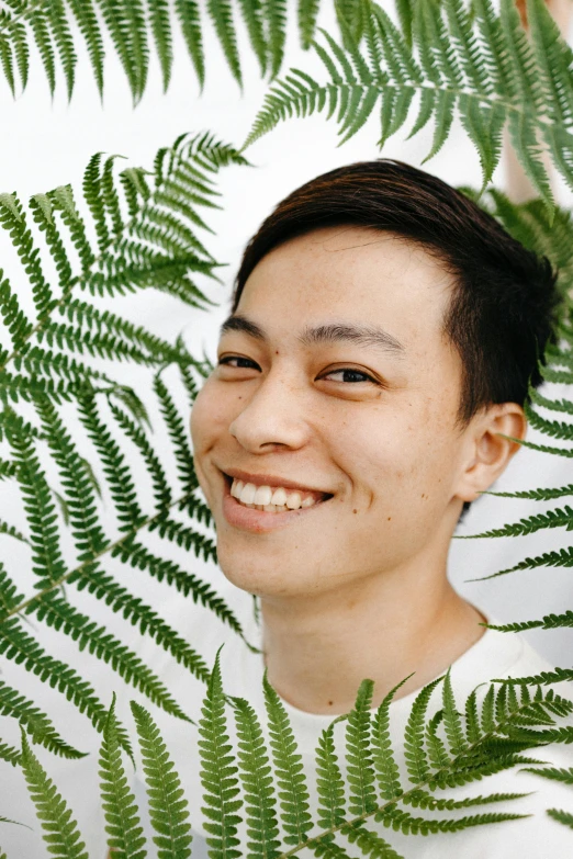 a man that is standing in front of a plant, inspired by Reuben Tam, pexels contest winner, sumatraism, androgynous face, smiling male, fern, in front of white back drop