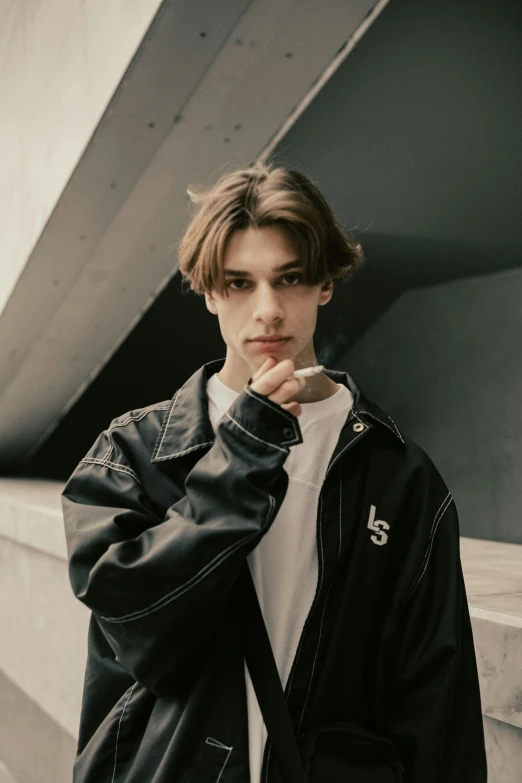 a man in a black jacket leaning against a wall, an album cover, inspired by Luca Zontini, trending on pexels, realism, beautiful androgynous girl, baggy, lv, thick jawline