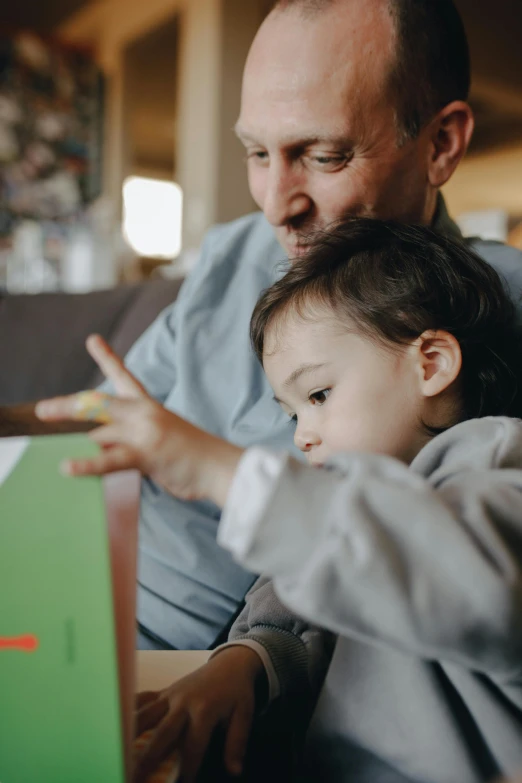 a man sitting next to a little boy on a couch, pexels contest winner, reading engineering book, gif, te pae, teaching