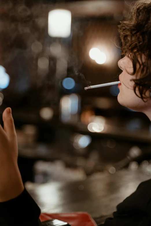 a woman sitting at a table with a cigarette in her mouth, inspired by Nan Goldin, pexels contest winner, happening, teen boy, drinking at the bar, finn wolfhard, profile image