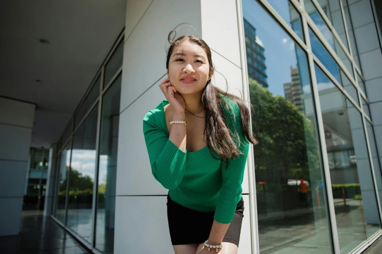 a woman leaning against a building talking on a cell phone, inspired by Cheng Jiasui, pexels contest winner, realism, wearing green clothing, young cute wan asian face, posing for a picture, student