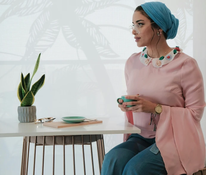 a woman sitting at a table with a cup of coffee, a colorized photo, inspired by Maryam Hashemi, trending on pexels, hurufiyya, teal headband, pink clothes, standing elegantly, arab ameera al-taweel