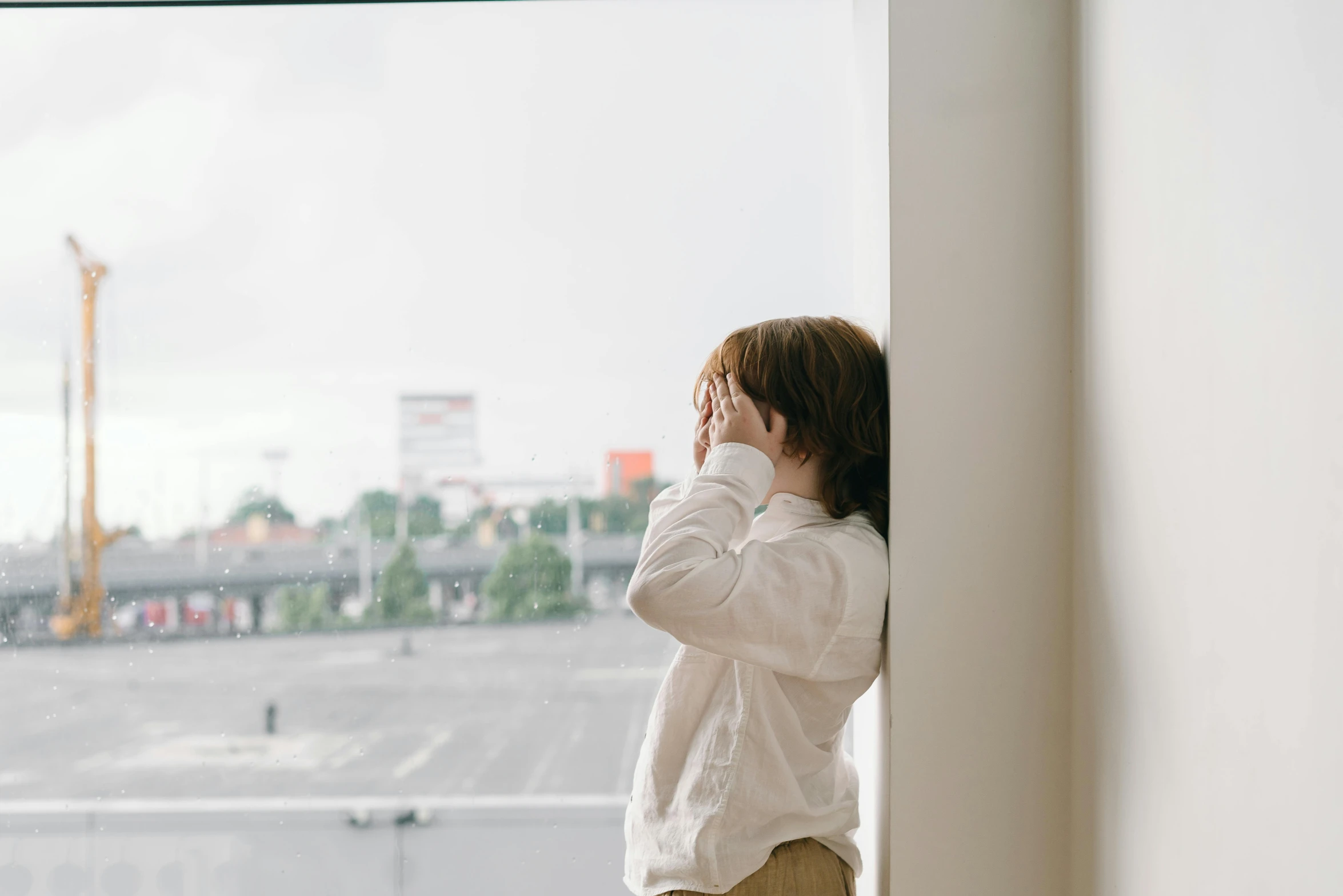 a woman standing in front of a window talking on a cell phone, a picture, by Emma Andijewska, trending on pexels, little boy, wearing a white shirt, background image, depressing image