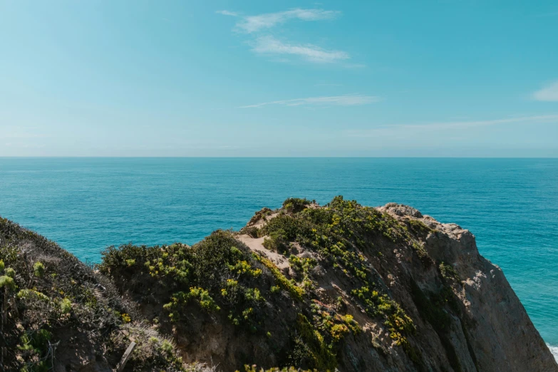 a man standing on top of a cliff next to the ocean, pexels contest winner, clear blue skies, thumbnail, teal aesthetic, te pae