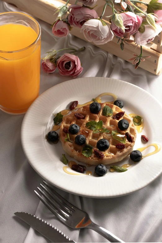 a white plate topped with waffles next to a glass of orange juice, renaissance, made of flowers and berries, eucalyptus, february)