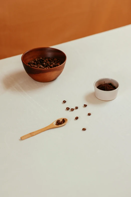 a white table topped with a bowl of coffee and a wooden spoon, inspired by Ceferí Olivé, renaissance, mineral grains, uncrop, press shot, long coffee brown hair