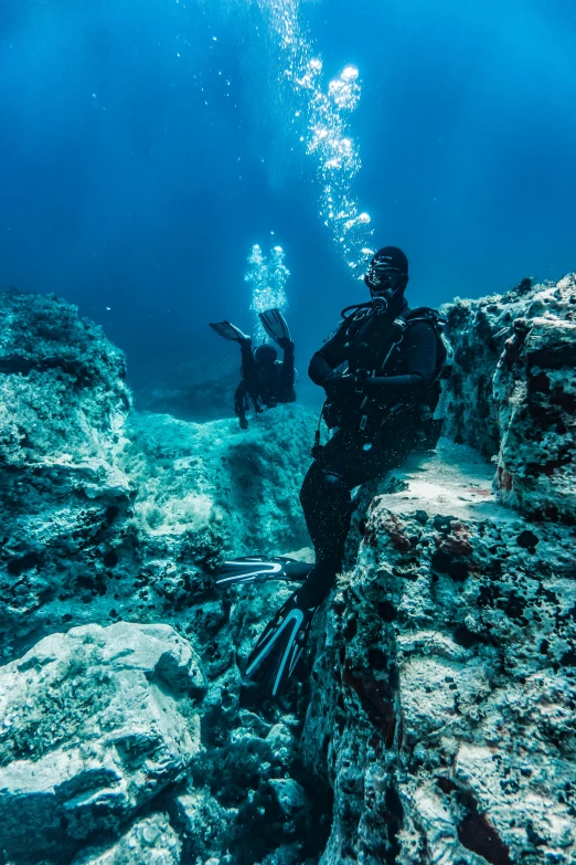 a couple of people that are standing in the water, reefs, sitting down, rocky terrain, scuba diving