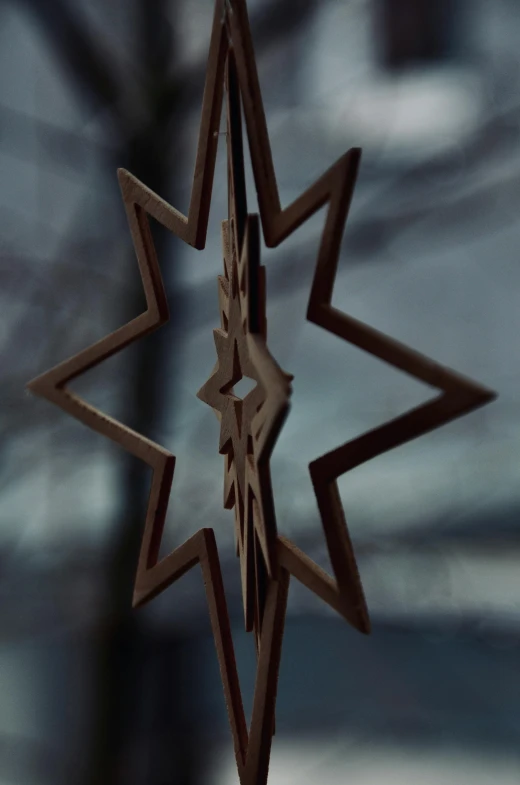 a wooden star ornament hanging from a window, an abstract sculpture, inspired by Rudolph F. Ingerle, unsplash, shot from cinematic, rotating, dark and forboding, profile image