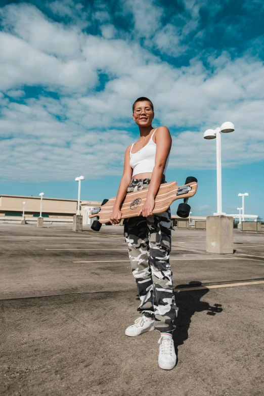 a man standing in a parking lot holding a skateboard, wearing a crop top, basia tran, wearing camo, standing on a cloud